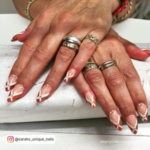 Brownish-Red White Tip Nails With Studs And Diamonds On White Table