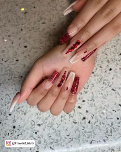 Coffin Red And White Nails Design With French Tips, Red Rhinestones, And Red Glitter On A Marble Surface