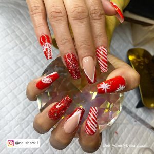 Coffine Red And White Acrylic Nail Ideas With Red Glitters, French Tips, Snowflakes, And Stripes Holding A Diamond Ball Over A Napkin