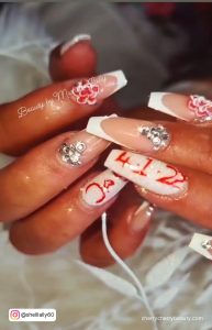 French Tips White And Red Coffin Nails With Rhinestones, Write-Ups, And Flowery Design On A Flowery Surface