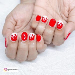 Hot, Fiery Red Nails With White Designs Of Fire Laying On A White Towel.