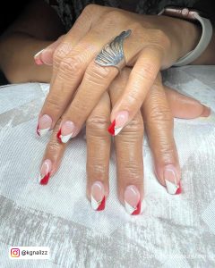 Red And White French Tips With Rhinestones On Each Nail Over A Nude Base With Nails Laying On Silvery Clothe
