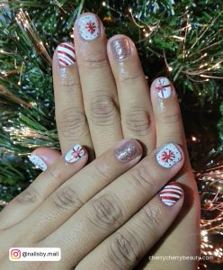 Short Glittery Red And White Christmas Nail Design With Diagonal Stripes, Snowflakes, And Gift Wrap Design Over Christmas Tree