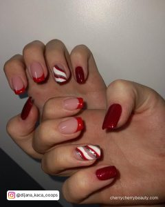 Short Red And White French Tip Nails With Swirly Stripes In Front Of A White Wall