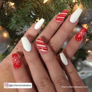 Striped Red And White Nails With Plain White Designs And Red With Snowflakes Design In Front Of Christmas Tree