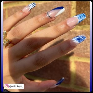Artsy Blue And White French Tip Nails With Multiple French Tip Designs Like Polka Dot, Snake Skin Design, Marbles, And Half Blue Half White French Tips Over Brick Wall Background