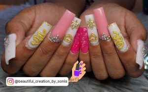 Blinge Pink, Gold, And White Acrylic Nails With Diamonds, Snake Desigb, And Glitters Over Marbles Surface