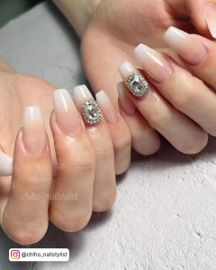 Cute Pink And White Ombre Nails With Diamonds Laying On White Surface