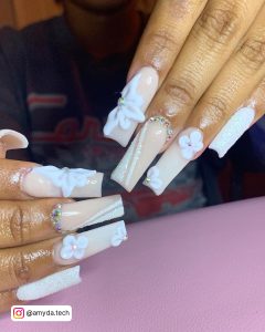 Cute White Acrylic Nail Ideas With Flower Design, Glitters, And Colorful Rhinestones Over Pink Surface