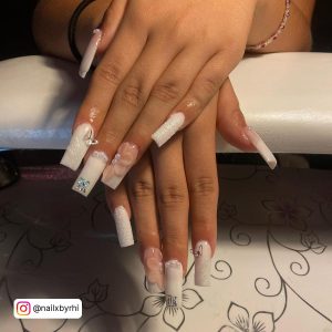 Cute White Glitter Acrylic Nails With Butterflies And Flower Design Over White Surface