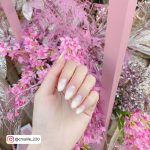 Cute White Ombre Almond Nails With Pink Flowers In Background