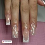 Double White French Tip Acrylic Nails With Glittery Swirly Design And Heart Design Over Pink Surface