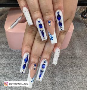 Fancy White And Glitter Silver Nails With Blue Rhinestones Over A Grey Carpeted Shelf