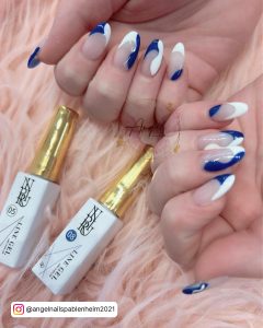 French Blue White Nails With Swirls Design Laying Beside Polish On A Peach-Colored Fur Clothe