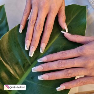 Half And Full White V Tip Nails With Glitter Laying On Leaf