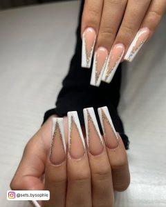 Hands With Long White Ombre Nails With French Glitter Lining Placed Over A White Shelf