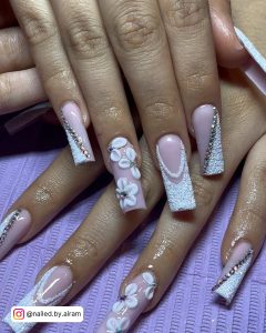 Long Coffin Acrylic Nails With Glitter, French Tips, Flower Design, And Rhinestones On Purple Surface.
