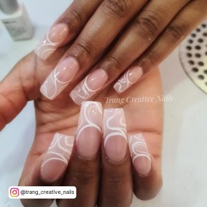 Long Nude Nails With White Tips And Swirly Design On A White Surface