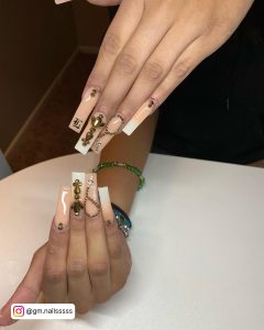 Long Square Rosery Nude And White Ombre Nails With Rosary And Cross Designs And Rhinestones Laying On White Surface