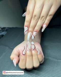 Long White Almond Nails With Brown Swirl Designs On Each Nail