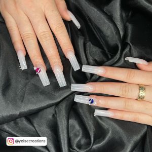 Long White Square Nails With Red, Blue And Silver Charms On Two Fingers