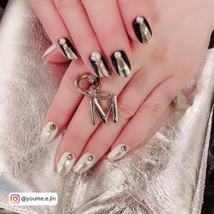 One Hand Of Black Nails With Metallic Silver Design With A Pearl On The Cuticle And One Hand With White Nails With Metallic Silver Design And Silver Gems
