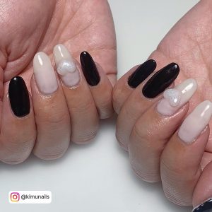Oval Black And White Gel Nails With Glittery White Heart Laying On White Surface