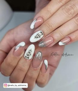 Oval French Tip Nails With Wavy White Tip And Silver Glitter Outline, A Silver French Tip And A White Feature Nail With Silver Gems