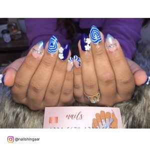 Royal Blue And White Nails With Rhinestones, Heart Art, And Swirly Tips Over Brown Fur