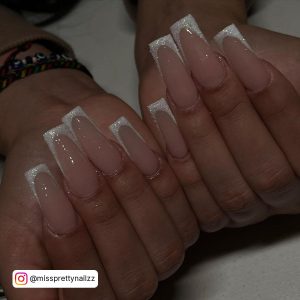 Shining Acrylic Nails With White Glitter Tips Placed Over A White Shelf