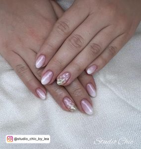 Shiny Round Tip Pink And White Ombre Nails With Gold Flakes And Leafy Design Over Laying On White Clothe
