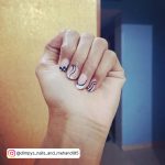 Short Checkered Black And White Gel Nails With Lines And Orange Wall In Background