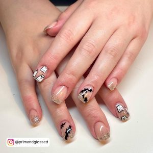 Short Gold Black White Glitter Nails With Ghost Art, Bat, And Glitter Designs Laying On White Surface