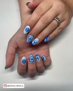 Short Oval Blue And White Acrylic Nails Design With Ying-Yang, Smiley Face, Fiery, And Heart Design Laying On White Surface
