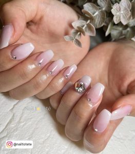 Short Pink White Ombre Nails With Diamonds On White Surface And With Leaves On The Palm