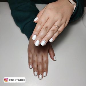 Short White Gel Nail Designs With Rhinestone On Ring Finger Nails Laying On A White Surface