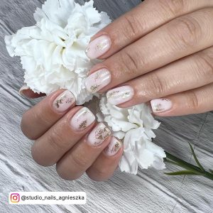 Short White Nails With Gold Glitter Holding A White Flower