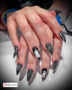 Spooky Halloween Black And White Stiletto Nails With Striped, Swirly, And Ghost Designs On White Surface