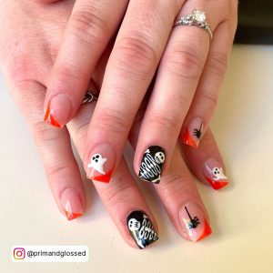 Spooky Res Black And White Nails With Half Red French Tips, Ghost And Skeleton Art, And Spider Design Laying On Cream Surface