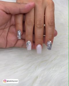 Square Tip Nails With Silver Glitter On Two Fingers And White Nails With A Silver Glitter Feature