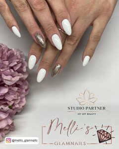 White Matte And Glitter Gold Almond Nails Near A Lilac Flower