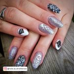 White Oval Nails With Black Designs On Three Fingers And Silver Glitter Nails On Two Fingers