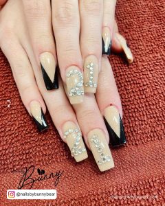 Beige Square Tip Nails With Black V Tips And 21 Written In Crystals Across Two Fingers