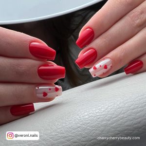 Square Tip Red Nails With Two Pearl White Nails With Red Hearts On Them