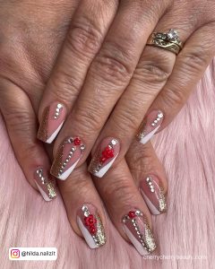 White Nails With Red Rhinestones On A Pink Surface