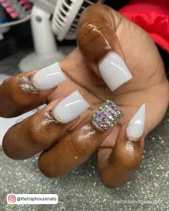 White Nails With Rhinestones On Ring Finger On Top Of A Silver Surface