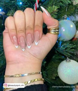 White Stiletto Nails With Rhinestones In Front Of A Christmas Tree