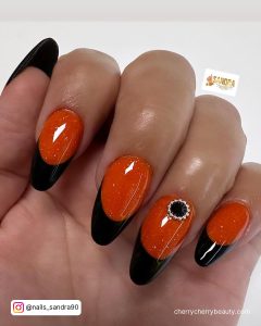 Bold Black French Tips Acrylic Nails With Sparkly Orange Base And Rhinestones And A White Background