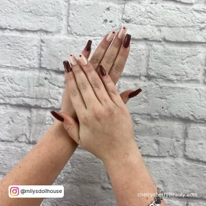Brown Acrylic Nails In Front Of A White Wall