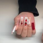 Coffin Baddie Red Acrylic Nails With Red Rhinestones And French Design On White Surface